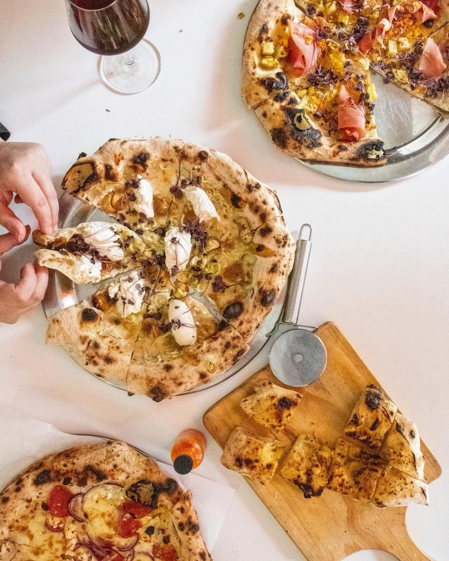 Mesa de jantar com várias pizzas napolitanas, focaccia e vinho na Tozzi Forneria Moderna, restaurante italiano no Saldanha, Lisboa